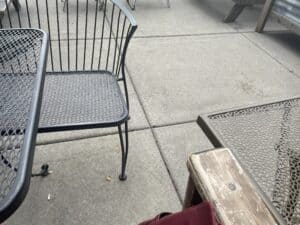 An image of a coffeeshop patio, made up of cement squares laid in a grid pattern with miscellaneous table and chairs.